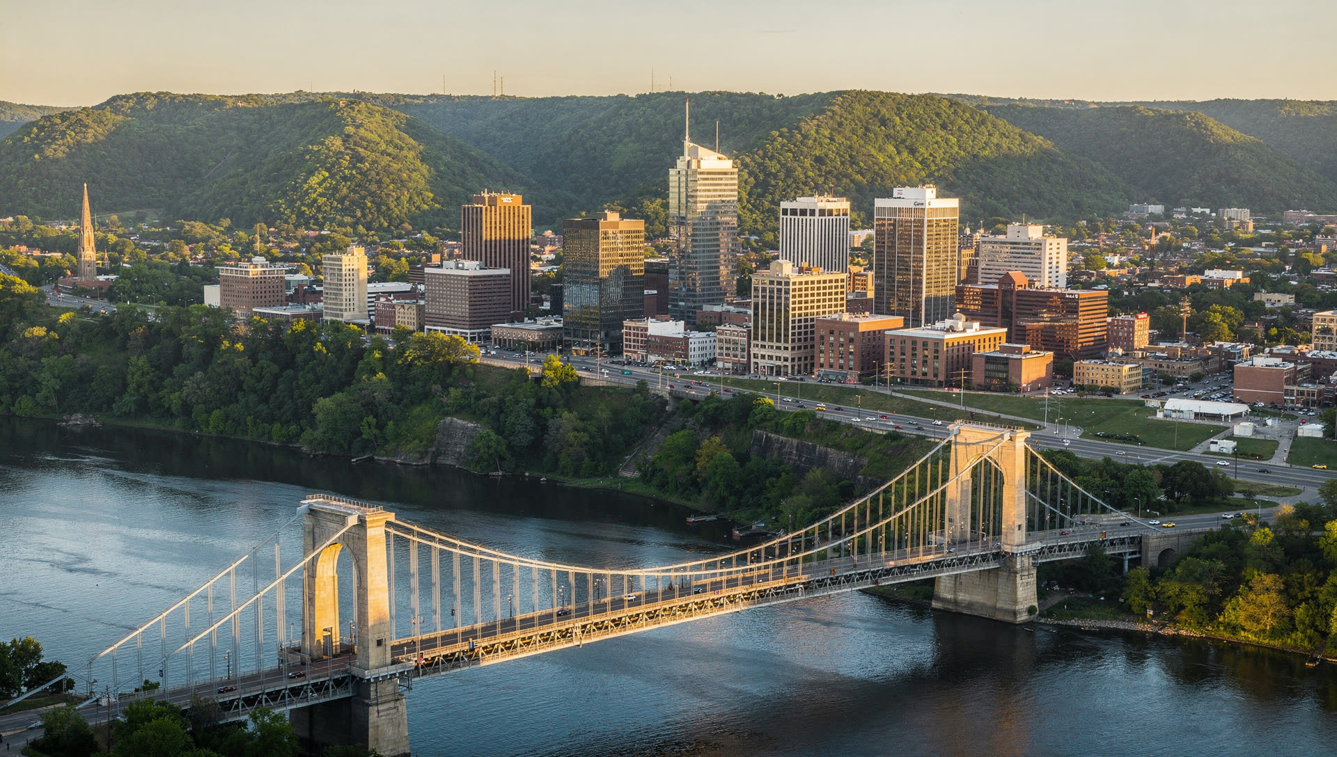 Aerial view of Cincinnati at golden hour, the downtown basin on the Ohio River with the bridges to Kentucky and the hillsides rising behind the city.
