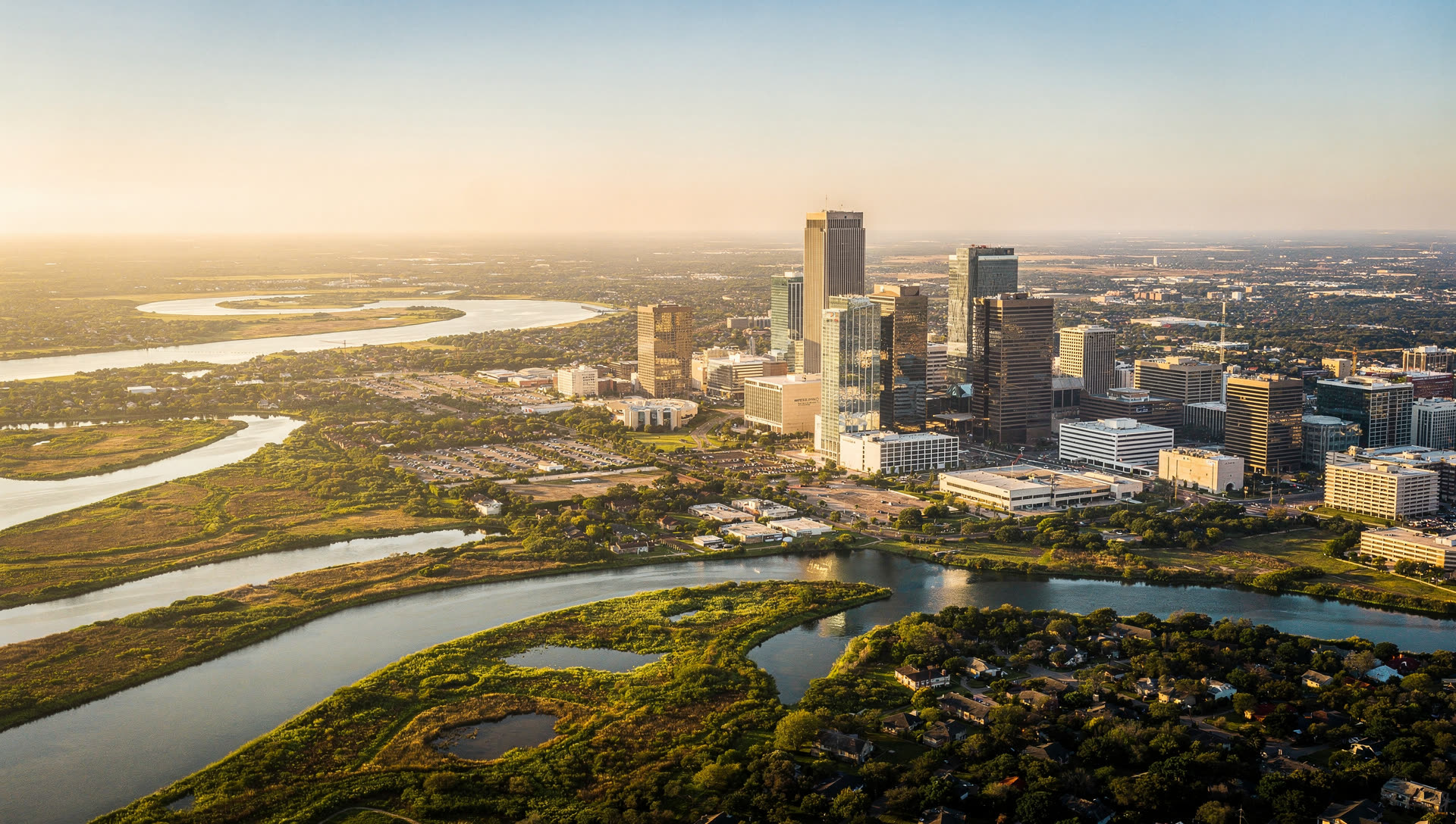 Aerial view of the Houston skyline at golden hour, downtown towers rising from a flat coastal plain with low-rise development spreading unbroken to the horizon in every direction.
