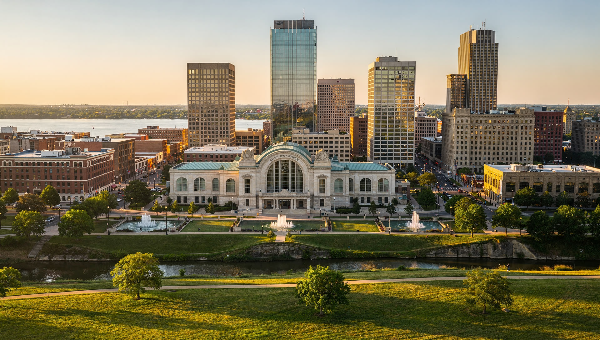 Aerial view of Kansas City at golden hour, the downtown skyline above the Missouri River with the street grid running west toward the Kansas state line.