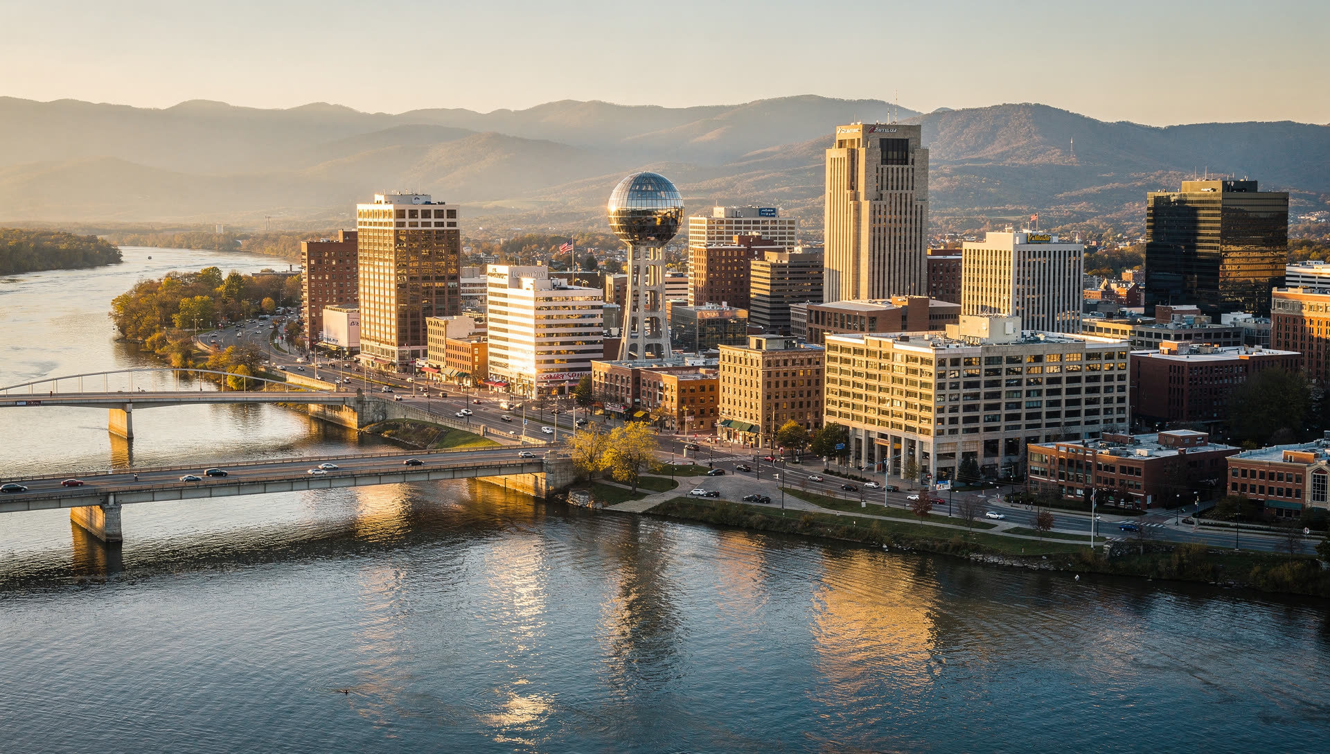 Aerial view of Knoxville at golden hour, the downtown skyline above the Tennessee River with the ridges of the Great Smoky Mountains in the distance.
