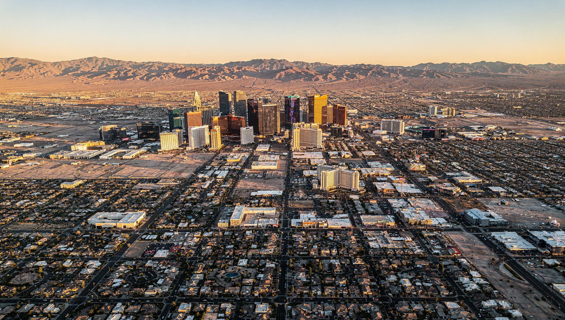 Aerial view of Las Vegas at golden hour, the Strip resort towers rising from the valley floor with the Spring Mountains along the western horizon.