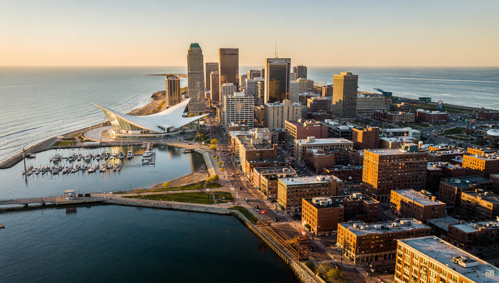 Aerial view of Milwaukee at golden hour, the downtown skyline on the Lake Michigan shore with the Milwaukee River and the Hoan Bridge to the south.