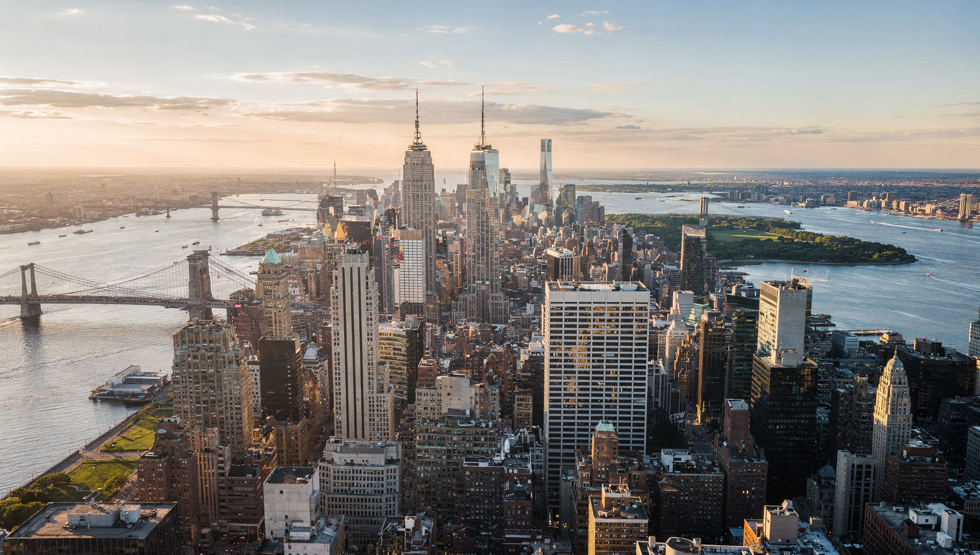 New York City from the air at golden hour, the Manhattan skyline with the East River bridges and the Brooklyn waterfront in the foreground.