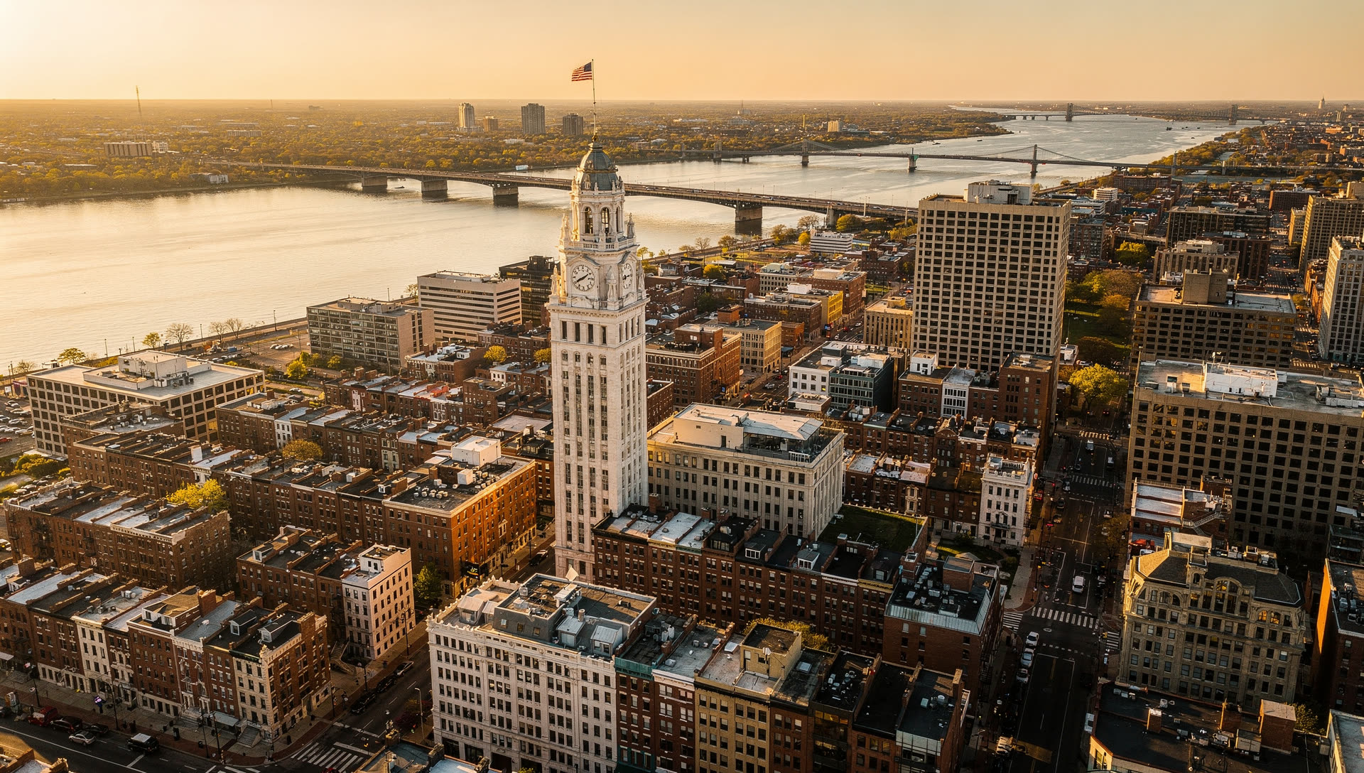 Aerial view of Philadelphia at golden hour, the Center City skyline with City Hall at the center and the Schuylkill River curving to the west.