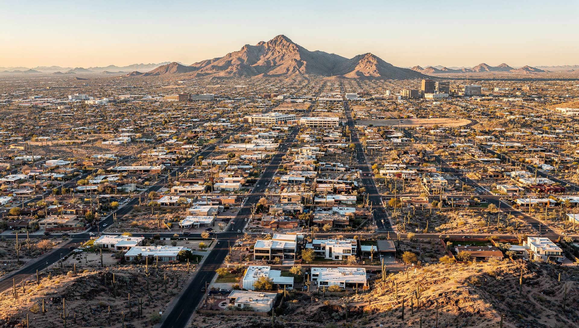 Phoenix, Arizona from the air at golden hour, the downtown towers with the Salt River valley spreading toward Camelback Mountain and the South Mountain ridge.