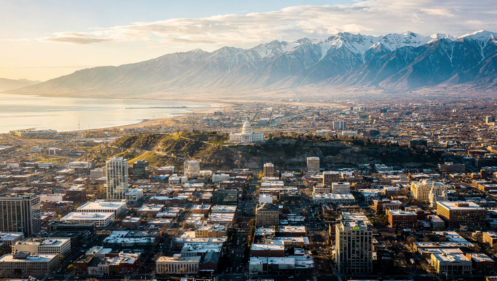 Aerial view of Salt Lake City at golden hour, the downtown grid and Utah State Capitol against the Wasatch Range with the valley floor spreading west toward the Great Salt Lake.