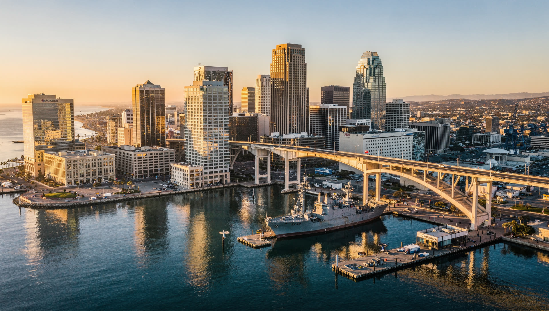 San Diego from the air at golden hour, the downtown towers on the bay with Coronado and the Pacific coastline stretching north.